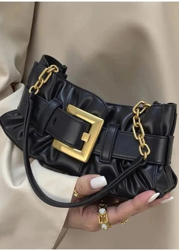 Black handbag with gold accents held by a person wearing a beige outfit.