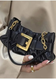 Black handbag with gold accents held by a person wearing a beige outfit.