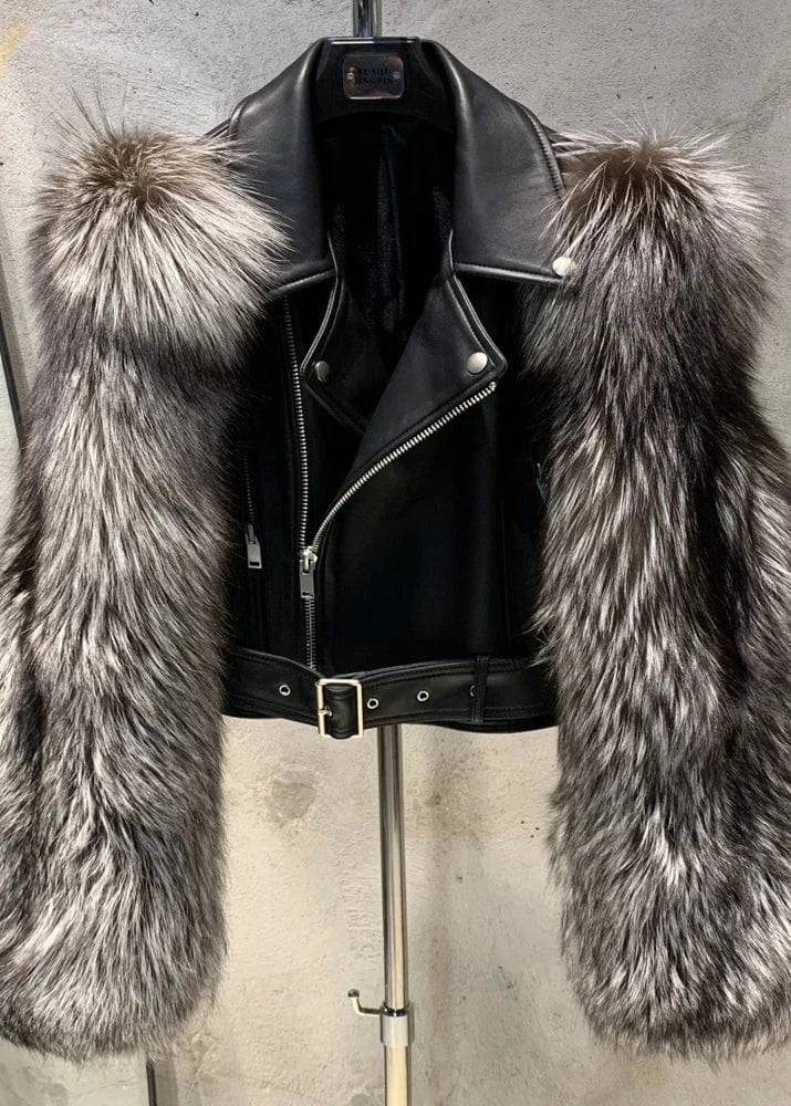 Black leather jacket with fur trim on a stand against a concrete wall.