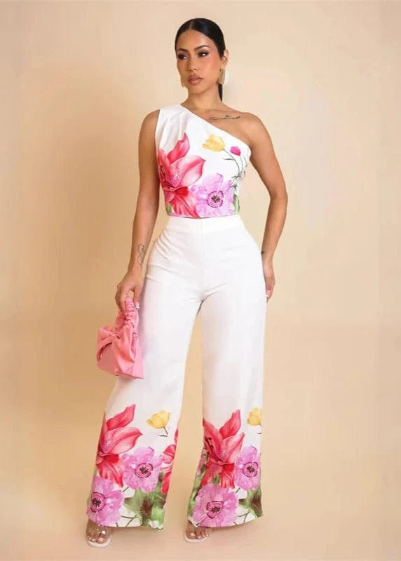 Woman wearing a floral one-shoulder top and white pants with a pink background