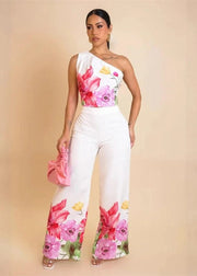 Woman wearing a floral one-shoulder top and white pants with a pink background