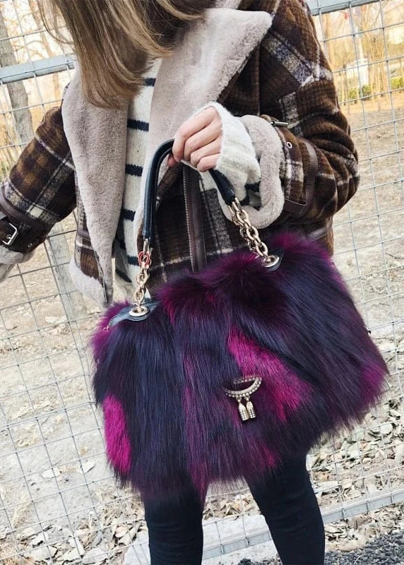 Person holding a purple fur handbag with a chain strap outdoors.