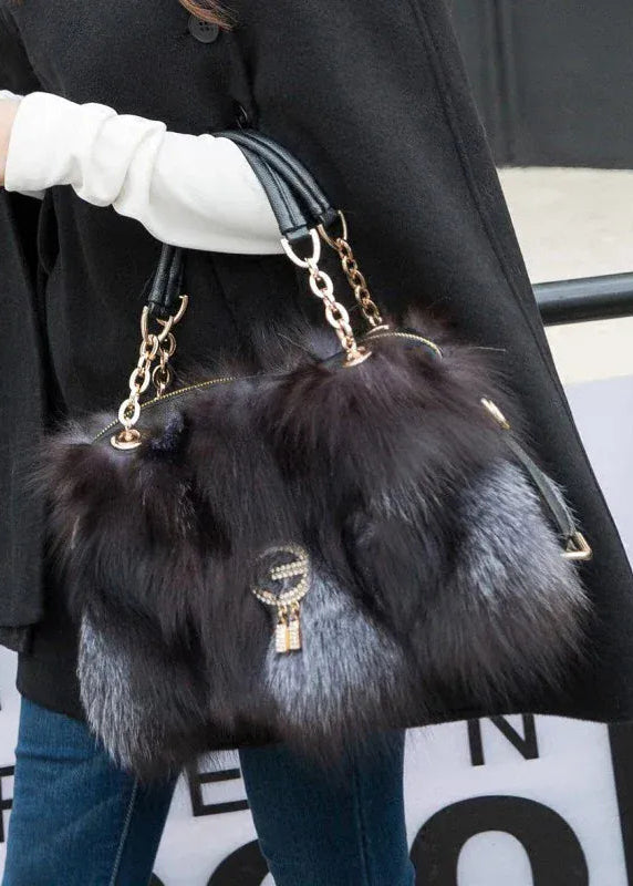 Person holding a black fur handbag with gold chain details