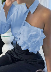 Person wearing a light blue off-shoulder top with floral details against a blurred outdoor background.