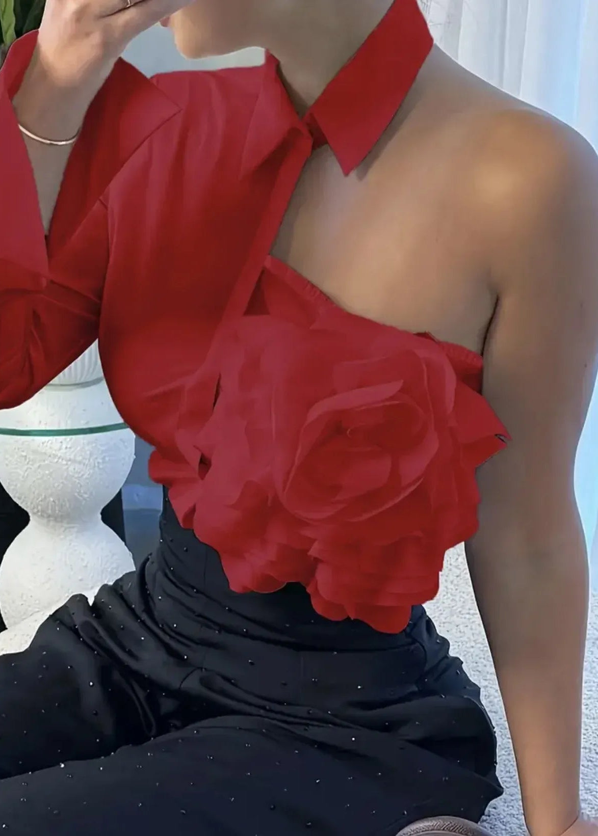 Person wearing a red halter top with a large flower detail, sitting outdoors.