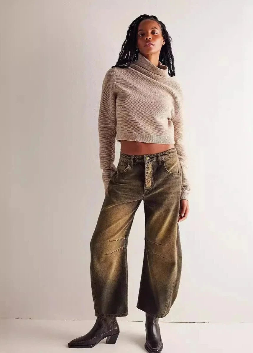 Person wearing a beige sweater and green pants against a plain background