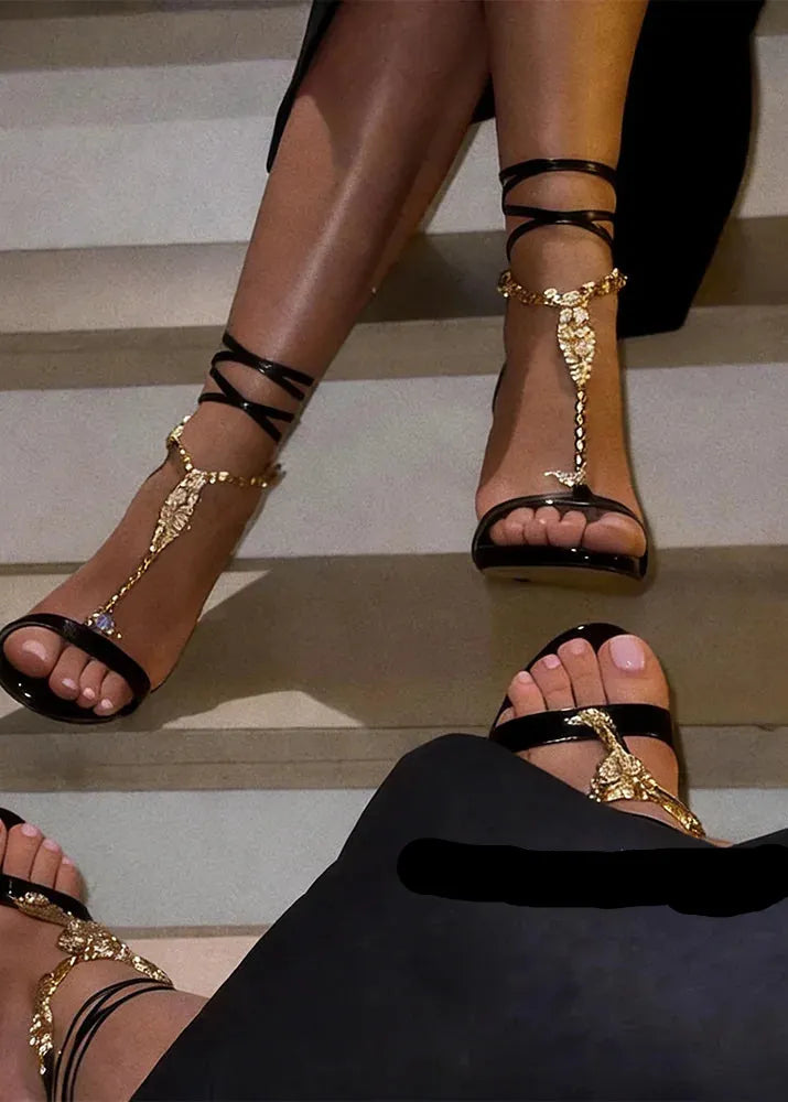 Black high-heeled sandals with gold straps worn by a person sitting on steps.
