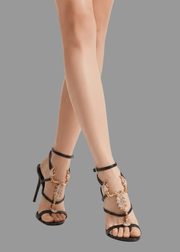 Black high-heeled sandals with gold accents worn by a person on a white background