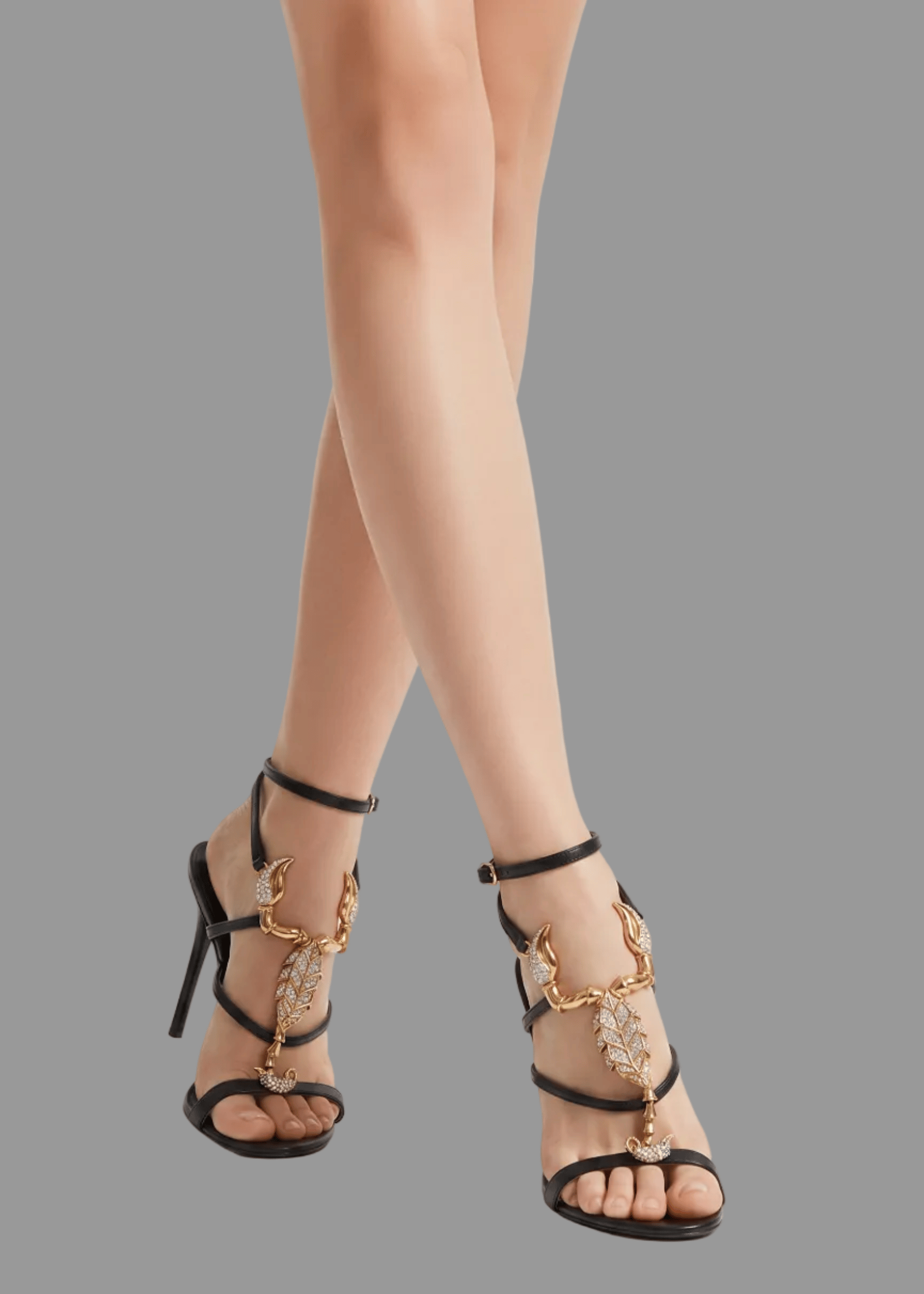 Black high-heeled sandals with gold accents worn by a person on a white background