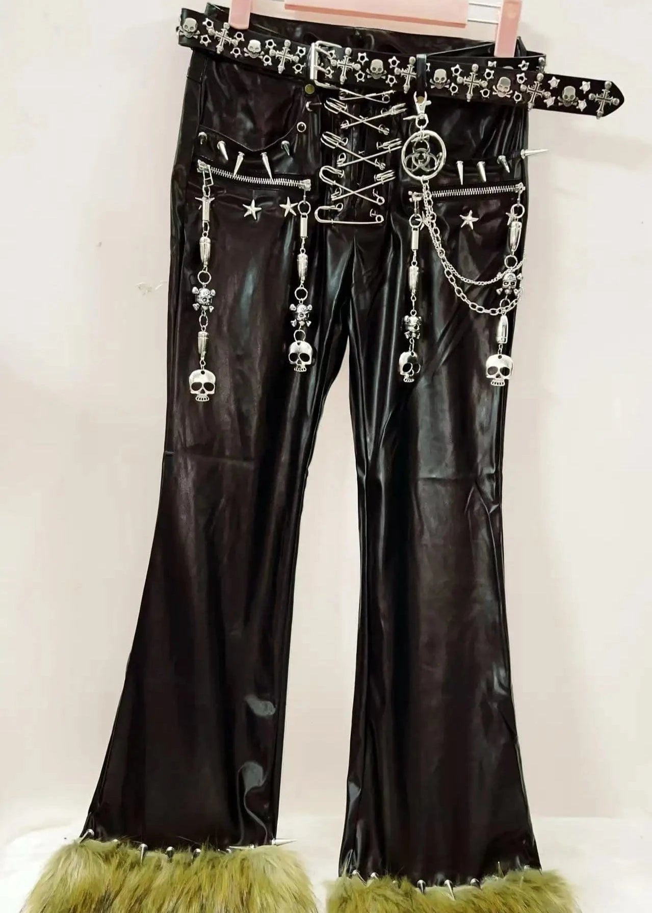 Black leather pants with decorative elements and green fringes on a white background