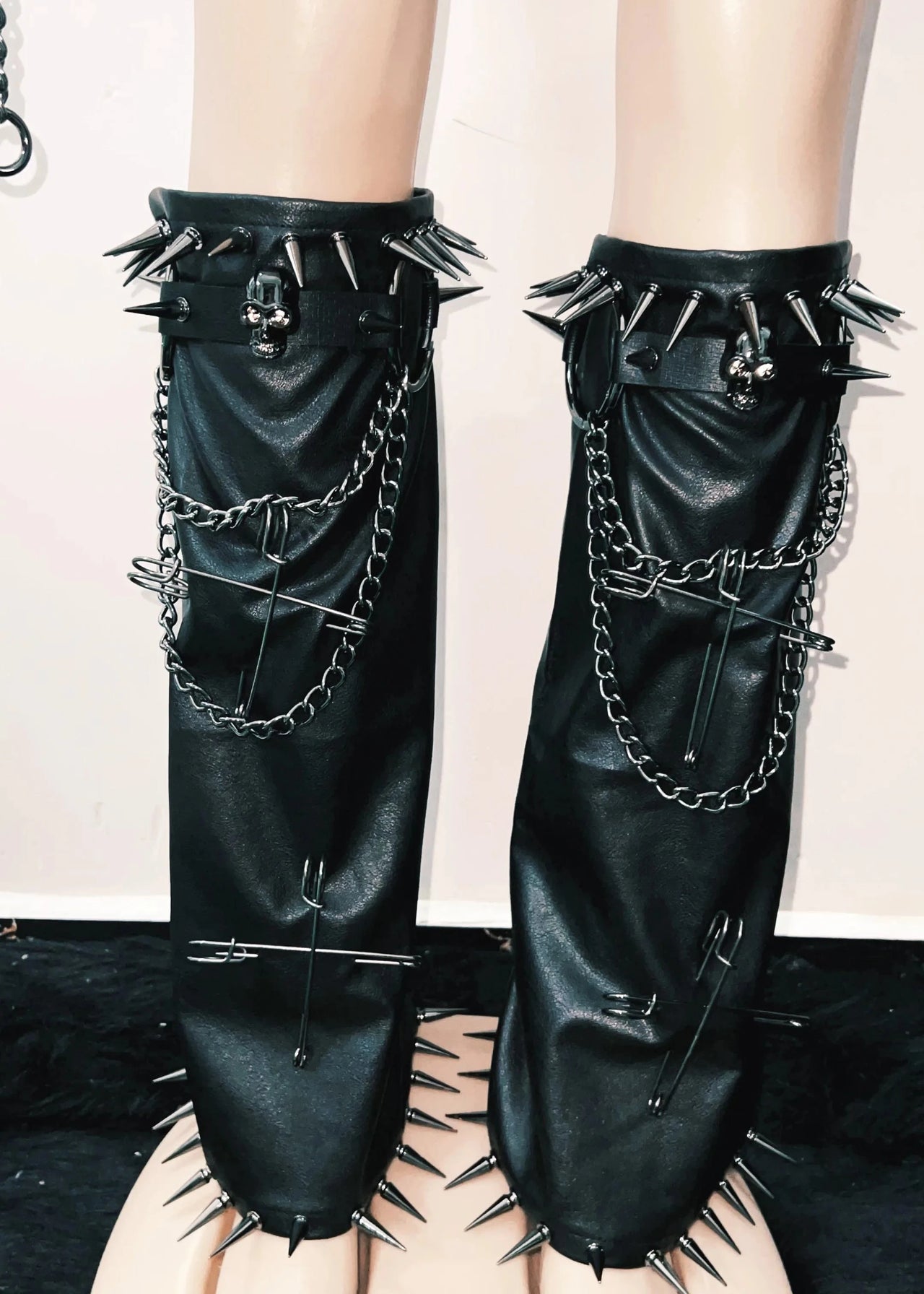 Black leather leg warmers with spikes and chains on a neutral background