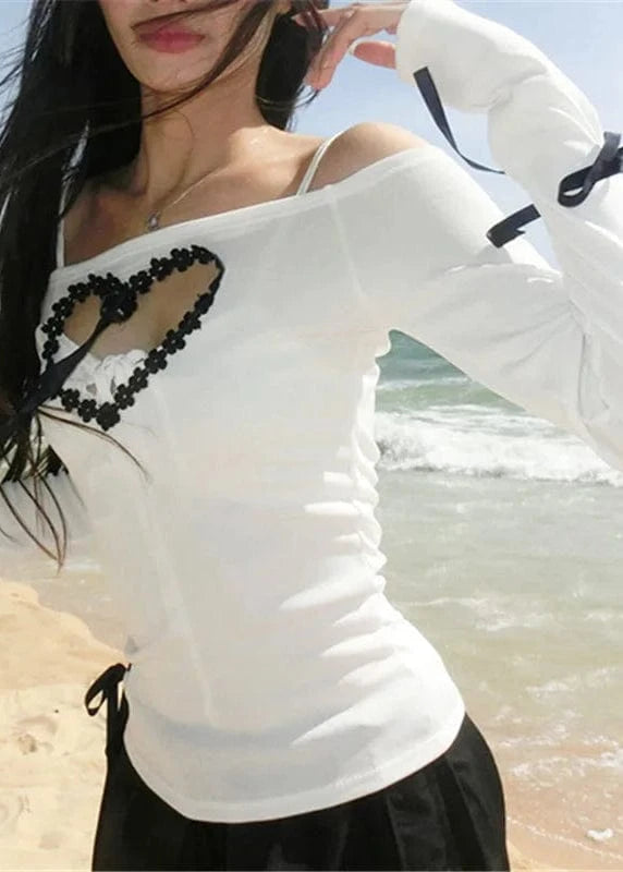 Woman wearing a white long-sleeve top with black heart design on a beach.