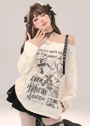 Person wearing a white oversized sweater with text and graphics, standing against a plain background