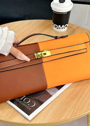 Two-tone brown and orange handbag held by a gloved hand on a wooden table with a coffee cup and magazine.