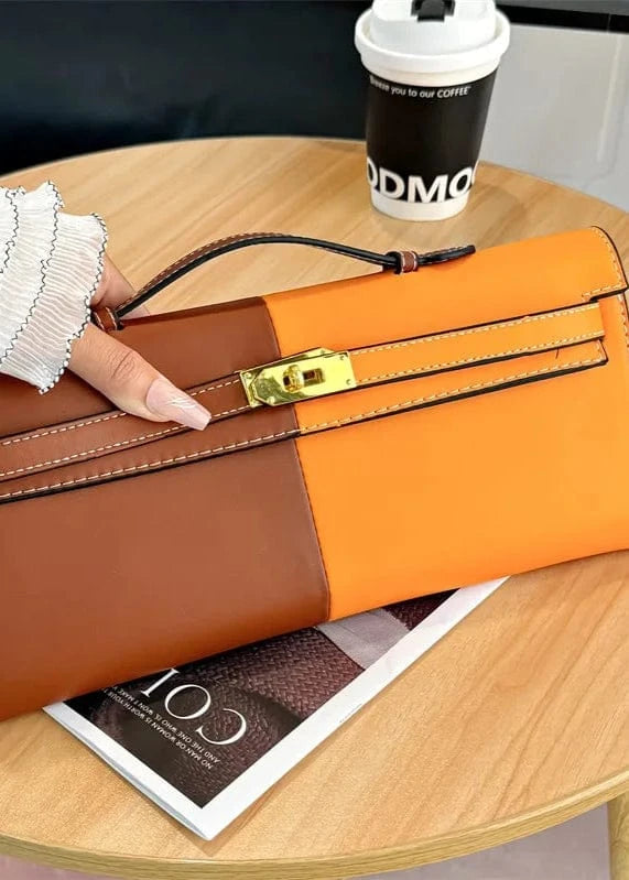 Two-tone brown and orange handbag held by a gloved hand on a wooden table with a coffee cup and magazine.