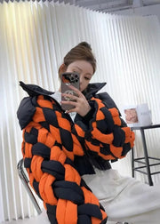 Person wearing a black and orange braided jacket in a room with white curtains.