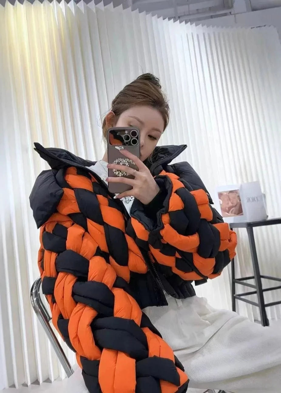 Person wearing a black and orange braided jacket in a room with white curtains.