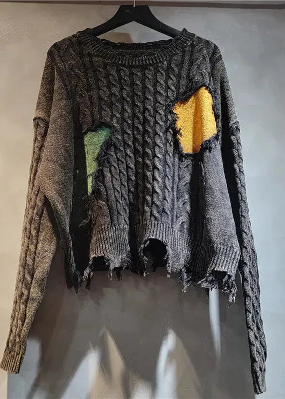 Ripped and distressed sweater with a yellow patch on a hanger against a plain wall.