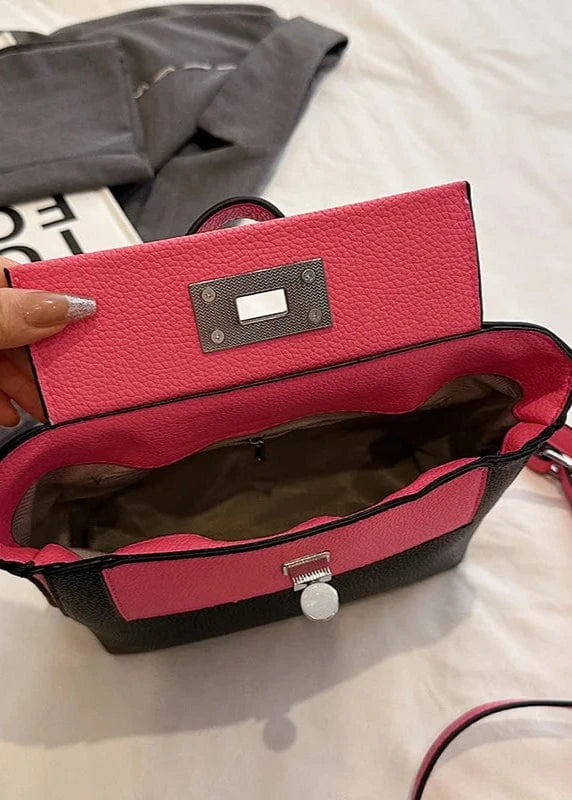 Red handbag with black interior held by a hand on a light-colored surface.