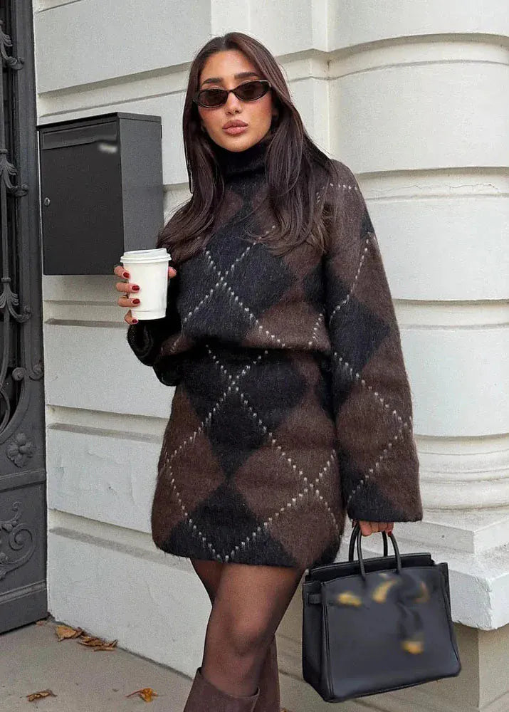 Woman in a patterned outfit holding a coffee cup and a black handbag, standing against a white wall.