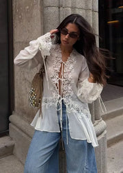 Woman wearing a white lace blouse and blue jeans standing on steps.