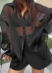 Person wearing a sheer black shirt over a dark outfit with a blurred background
