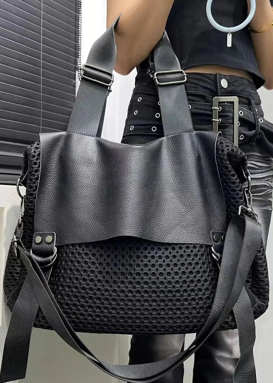 Black leather handbag with perforated design held by a person against a neutral background