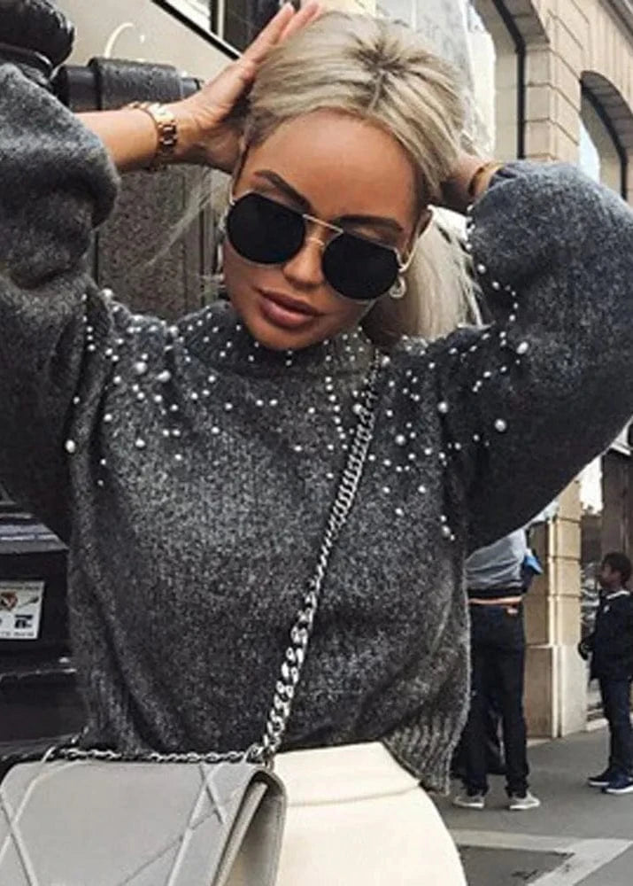 Person wearing a sparkly gray sweater with sunglasses and a handbag on a city street.