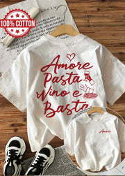 White t-shirt with red text 'Amore Pasta Wino e Basta' on a wooden surface with shoes and a baby bib.