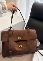 Brown suede handbag with gold clasp held by a person indoors.