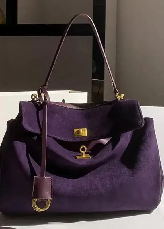 Purple handbag with gold accents on a white surface