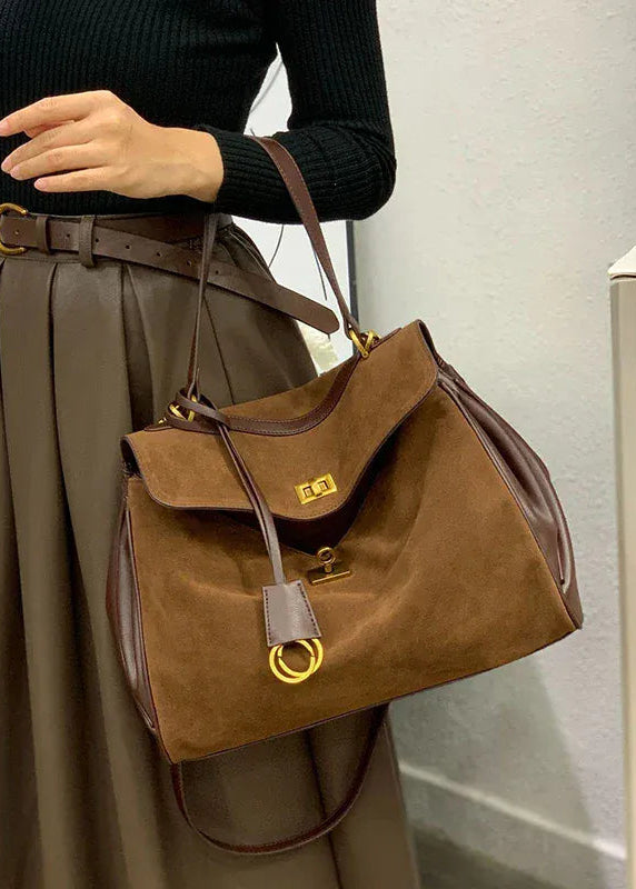 Person holding a brown handbag with a gold clasp in an indoor setting