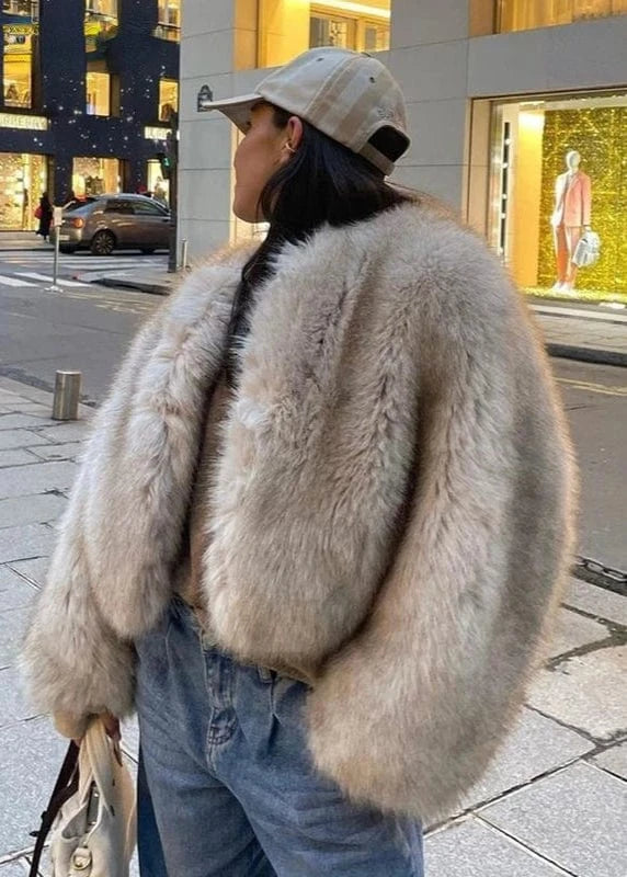 Person wearing a fur coat and cap on a city street with store windows in the background