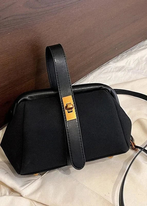 Black handbag with a gold clasp on a white fabric background