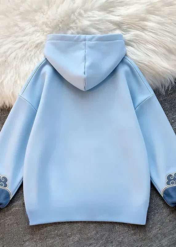 Light blue hoodie with cloud designs on cuffs and hem, placed on a textured surface.