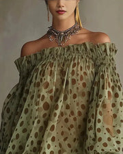 Woman wearing a green off-shoulder top with brown polka dot pattern against a neutral background