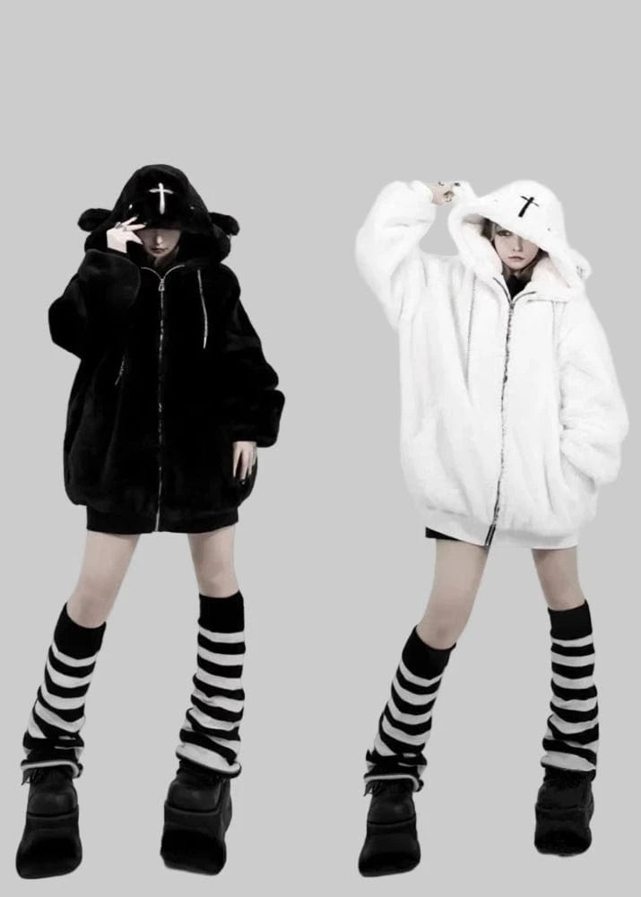 Two people wearing black and white hoodies with striped socks and black shoes on a plain background.
