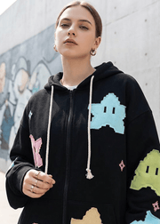Person wearing a black hoodie with colorful graphics against a graffiti-covered wall.
