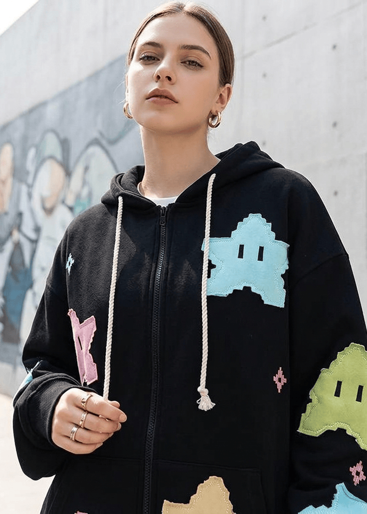Person wearing a black hoodie with colorful graphics against a graffiti-covered wall.