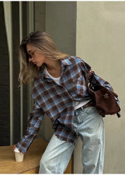 Woman in plaid shirt and jeans with a brown bag, standing by a wooden table.