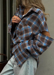 Person wearing a plaid shirt with rolled-up sleeves against a neutral background