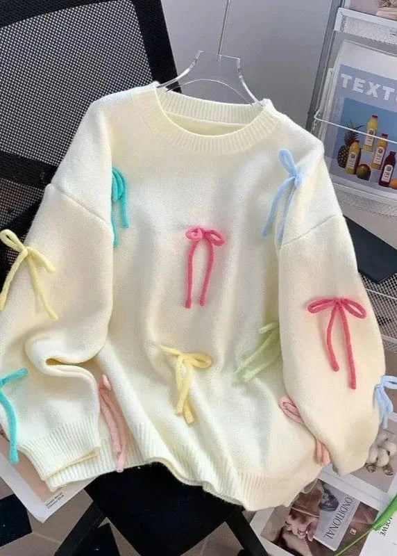 Light-colored sweater with colorful bows on a hanger against a magazine background