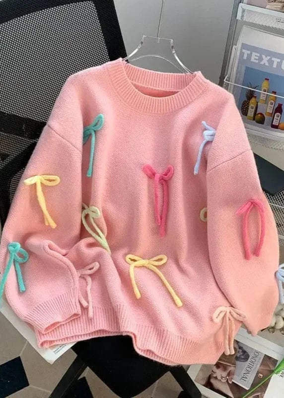 Pink sweater with colorful bows on a hanger against a magazine background