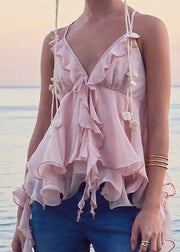 Woman wearing a pink ruffled top with a blurred beach background