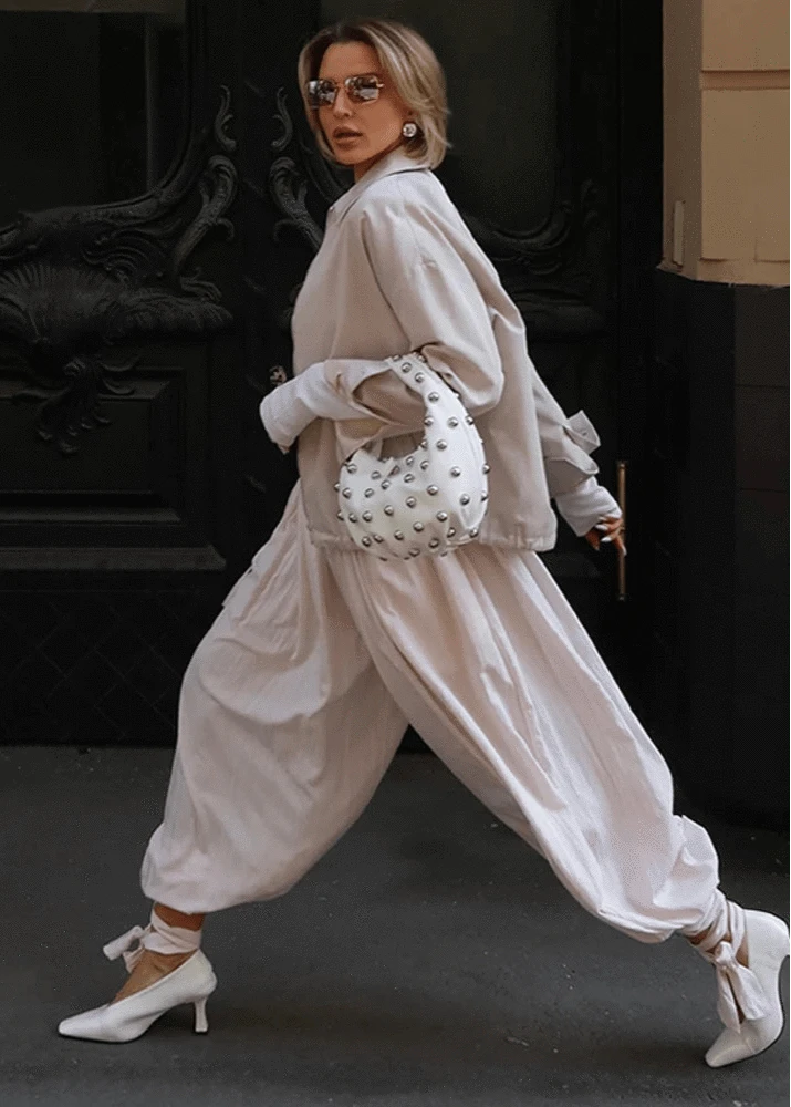 Woman in a stylish outfit with a white studded handbag against a dark background