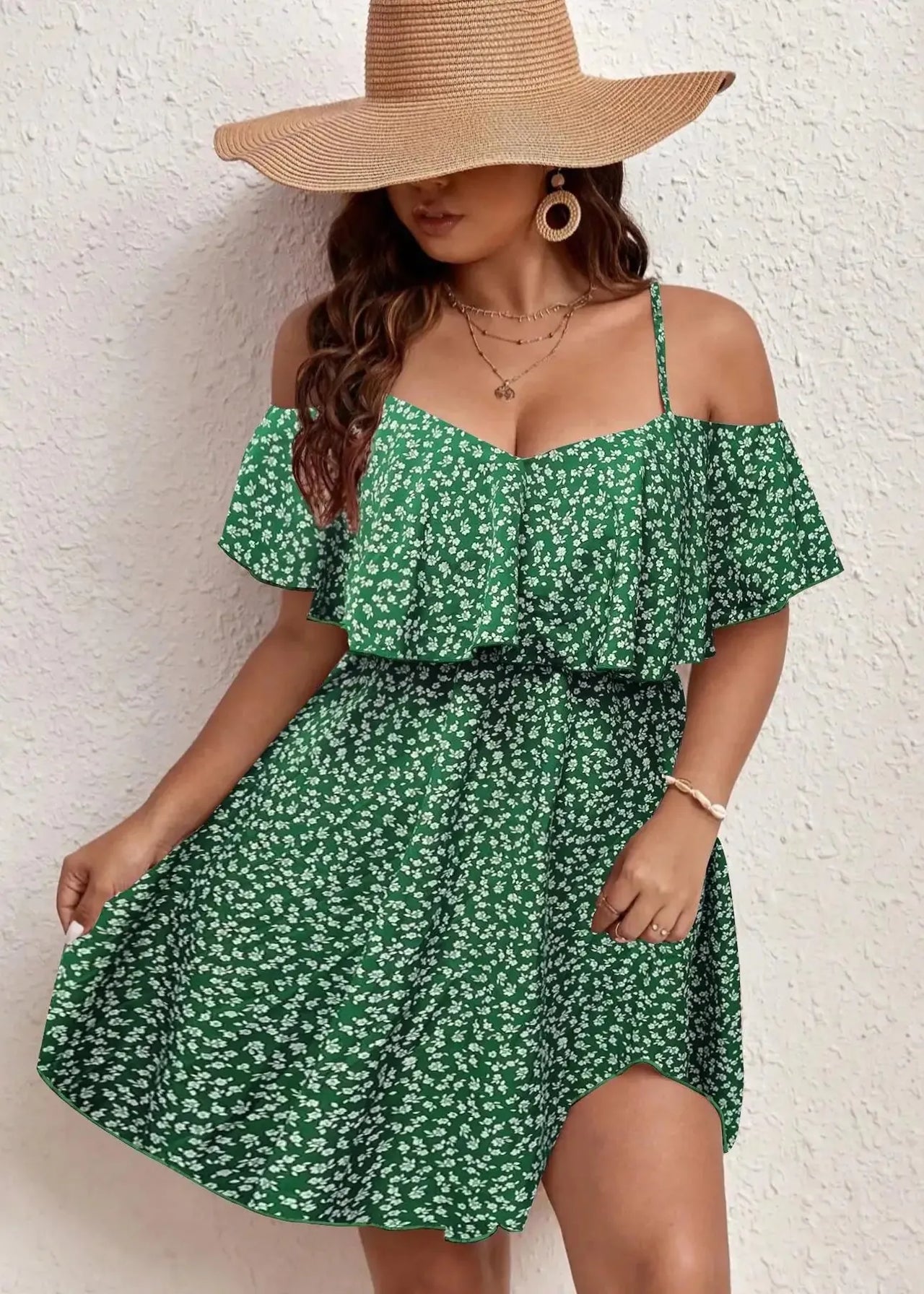 Woman wearing a green floral dress and wide-brimmed hat against a white wall