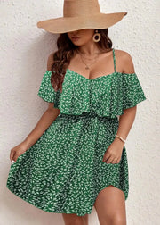 Woman wearing a green floral dress and wide-brimmed hat against a white wall