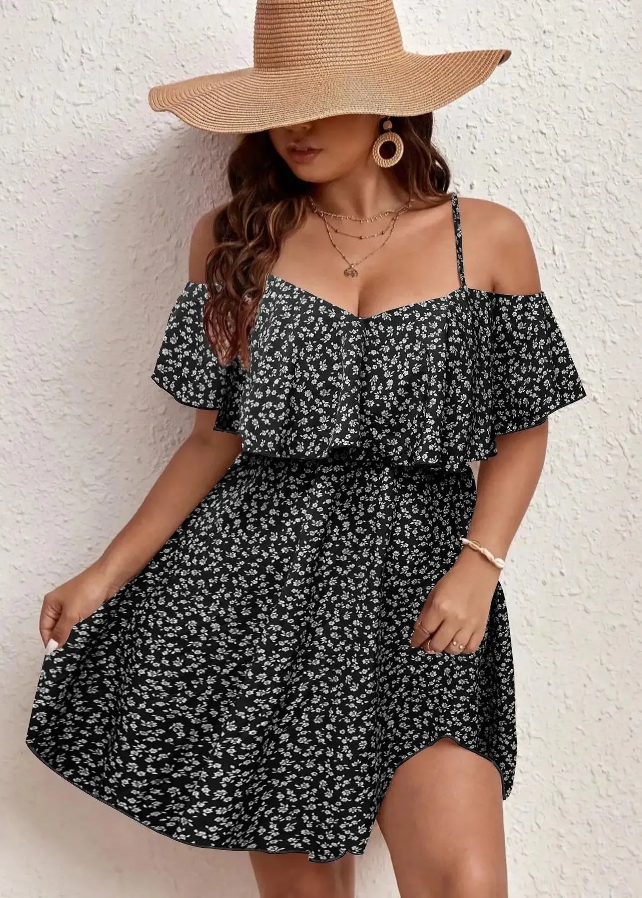 Woman wearing a black floral dress and wide-brimmed hat against a white wall