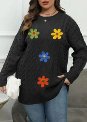 Person wearing a black sweater with colorful flower patterns against a white wall.