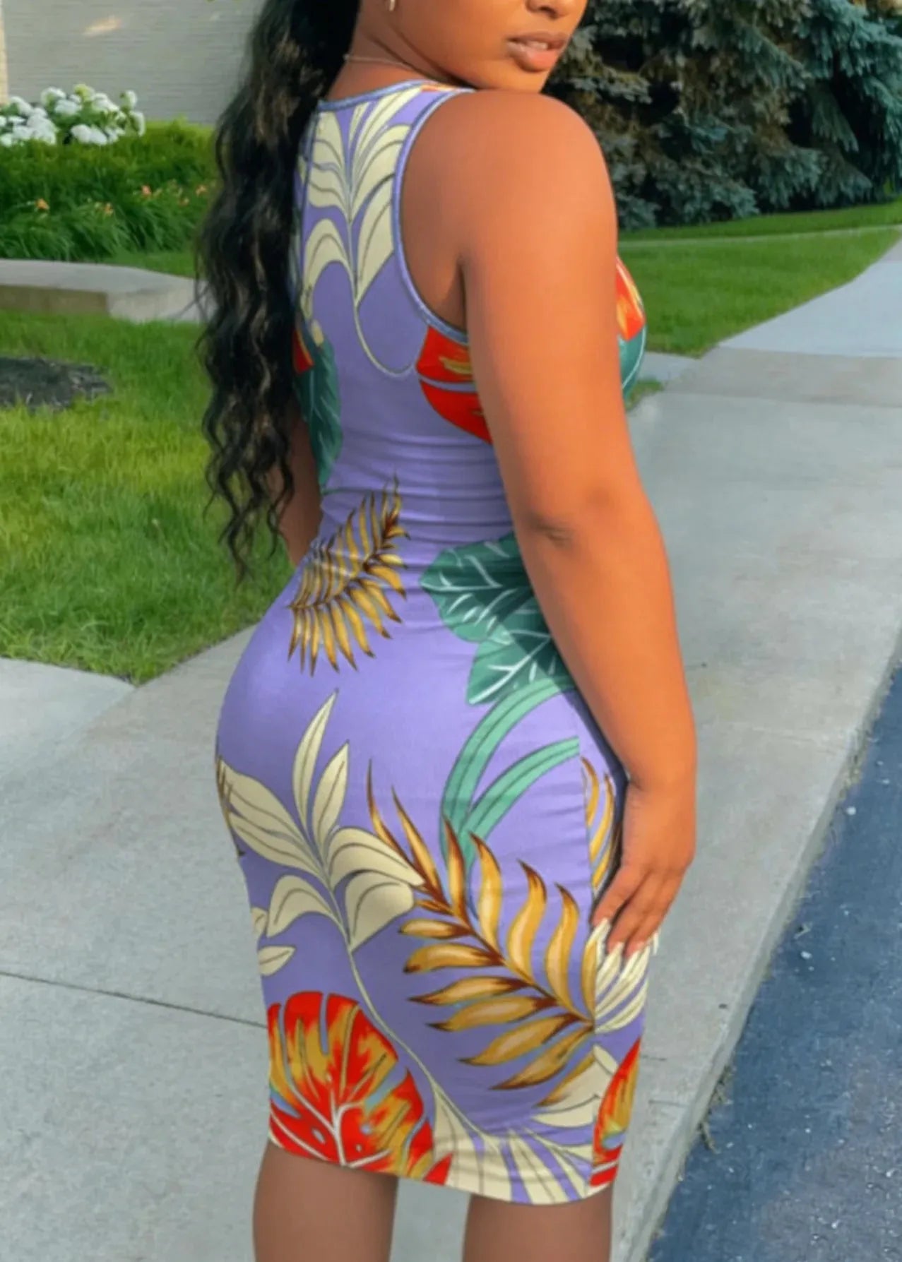 Woman wearing a colorful dress with leaf patterns on a sidewalk.